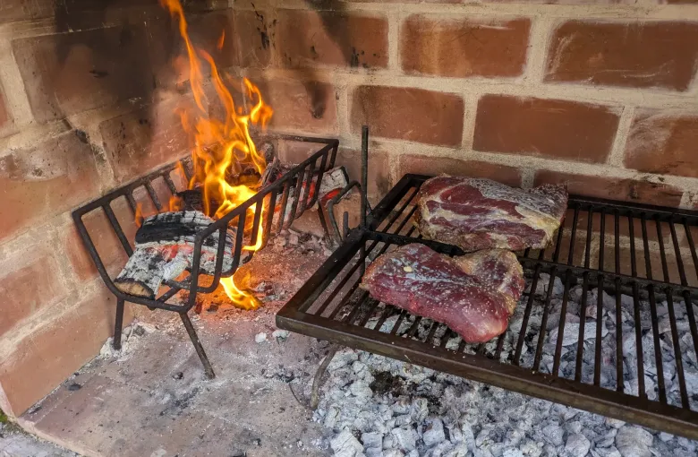 Cuts of beef cooking slowly on a grill above wood coals at a traditional Argentine asado.