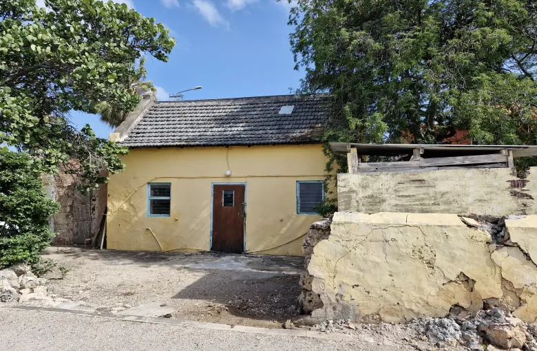 A traditional yellow cunucu house with a tiled roof and a low stone wall in Oranjestad, Aruba.