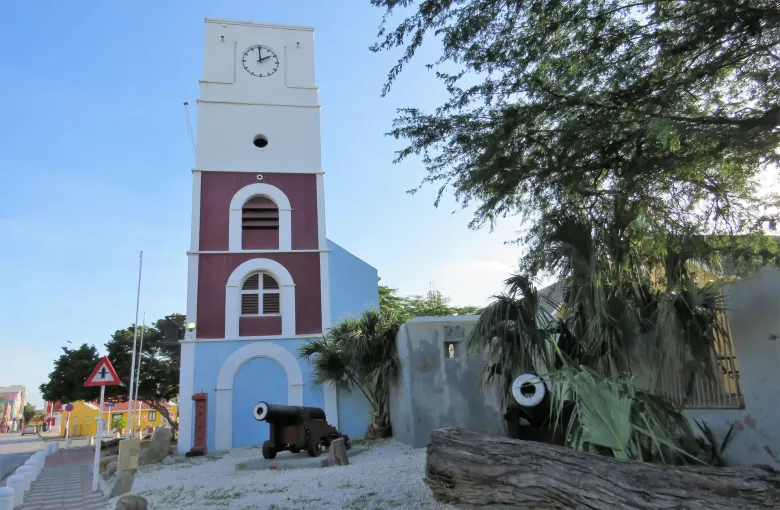 The red and white Willem III Tower at Fort Zoutman in Oranjestad, with cannons on the ground below.