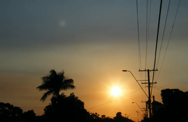 The sun showing as a pale disc through thick bushfire haze above suburban trees and rooftops.