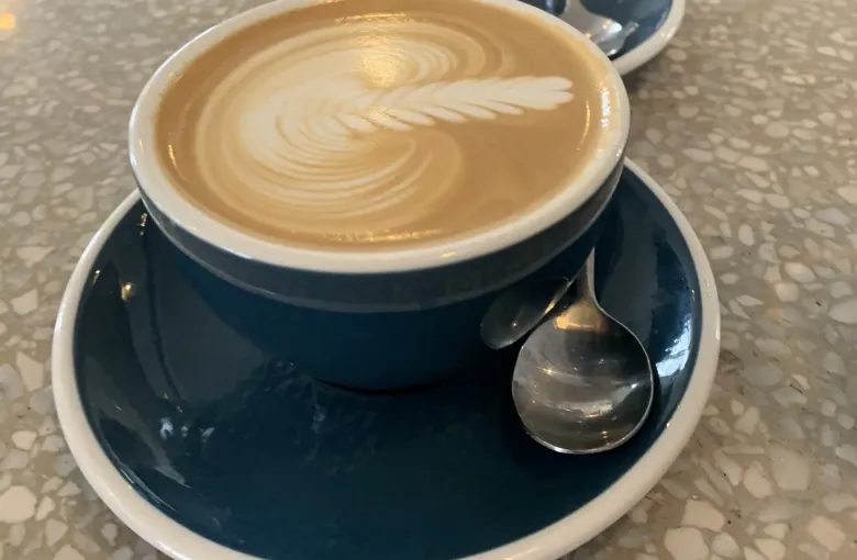 A flat white coffee with poured latte art, seen from above on a stone cafe counter.