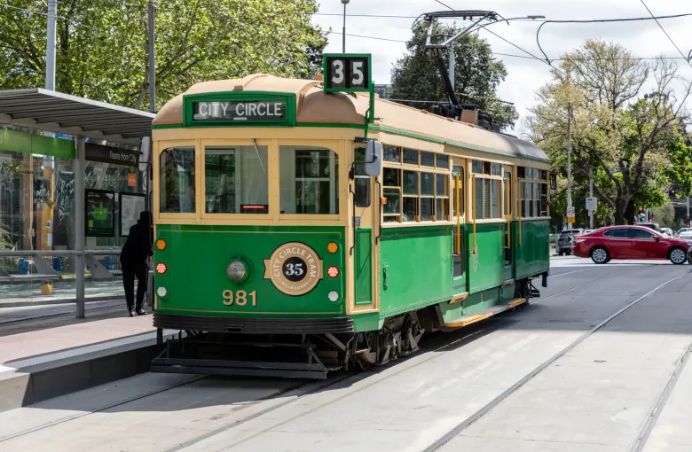 A green and gold City Circle heritage tram waiting at a street stop in central Melbourne.