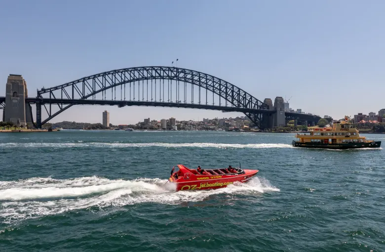 A Sydney ferry crossing the harbor in front of the Harbour Bridge on a bright day.