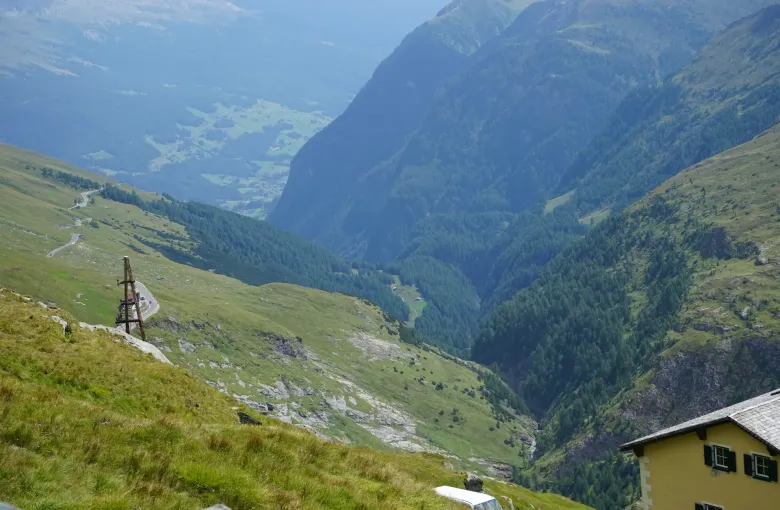 A broad Austrian alpine valley in late summer, green to the treeline with a farmhouse on the slope and bare rock above.
