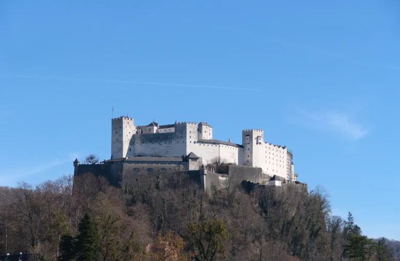 The white walls of the Hohensalzburg fortress on its wooded ridge under an unbroken blue sky.
