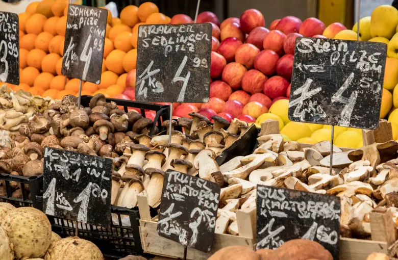 Mushrooms, oranges, apples and lemons banked up on a Naschmarkt stall in Vienna behind chalked price signs written in German.