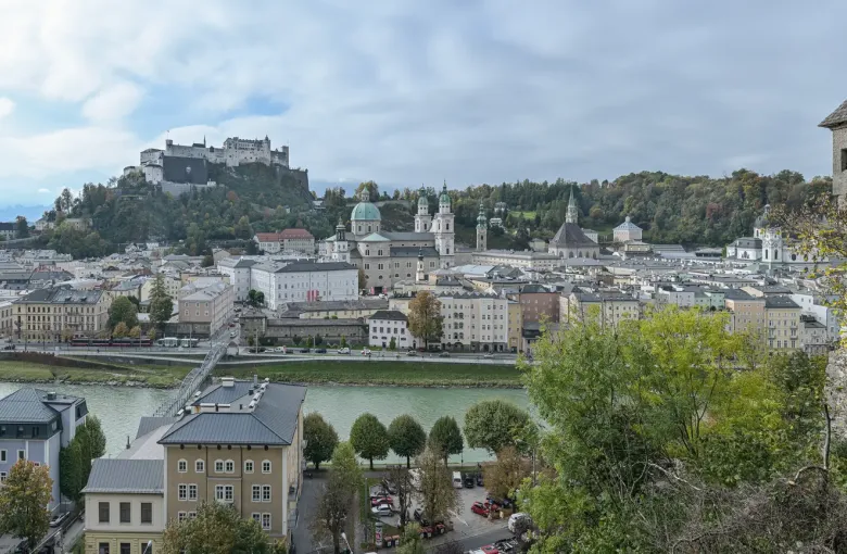 The domes and roofs of the historic centre of Salzburg along the Salzach river, with the Hohensalzburg fortress on the ridge above.