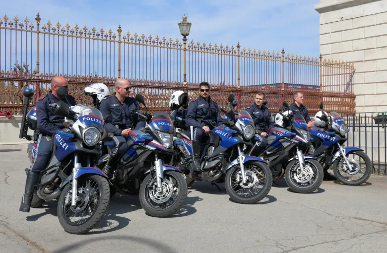 A line of Austrian police motorcycles with their riders drawn up beside a gilded railing in central Vienna.