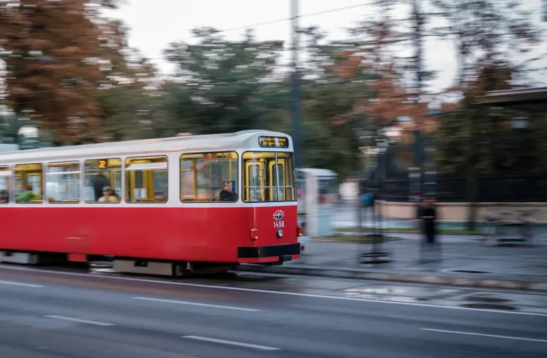 A red and white Vienna tram photographed in motion along a city street, the background blurred by the panning.