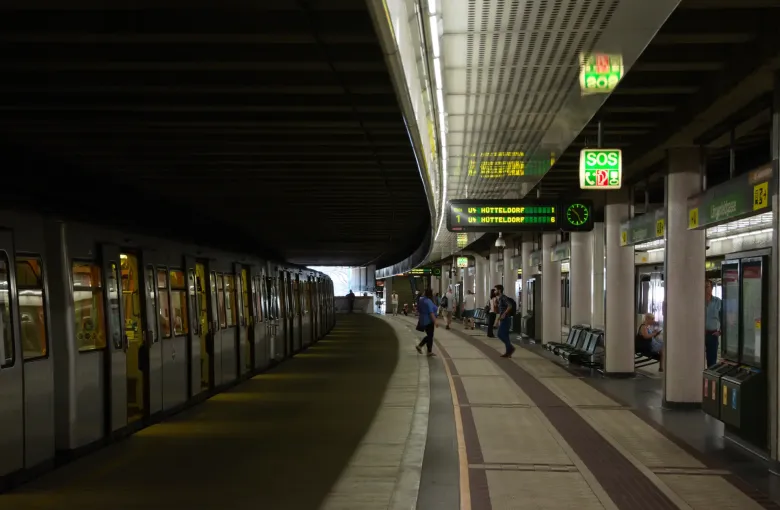 A Vienna U-Bahn platform with benches along its length, a train waiting at the left and departure indicators overhead.