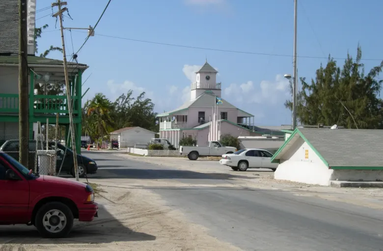 A quiet sand-edged street in Matthew Town, Great Inagua, with parked pickups, a taxi sign and the flag flying.