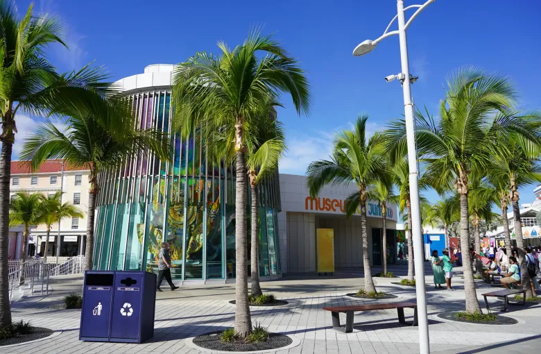 A tall Junkanoo costume behind the glass rotunda of the Museum of Junkanoo in Nassau, framed by palms.