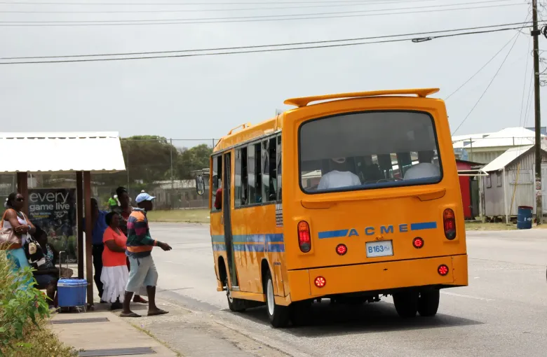 A bright yellow privately owned minibus picking up passengers at a roadside stop in Speightstown.