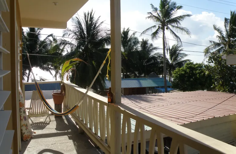 A hammock slung on a shaded wooden veranda on Caye Caulker, looking out past palms to the sea.