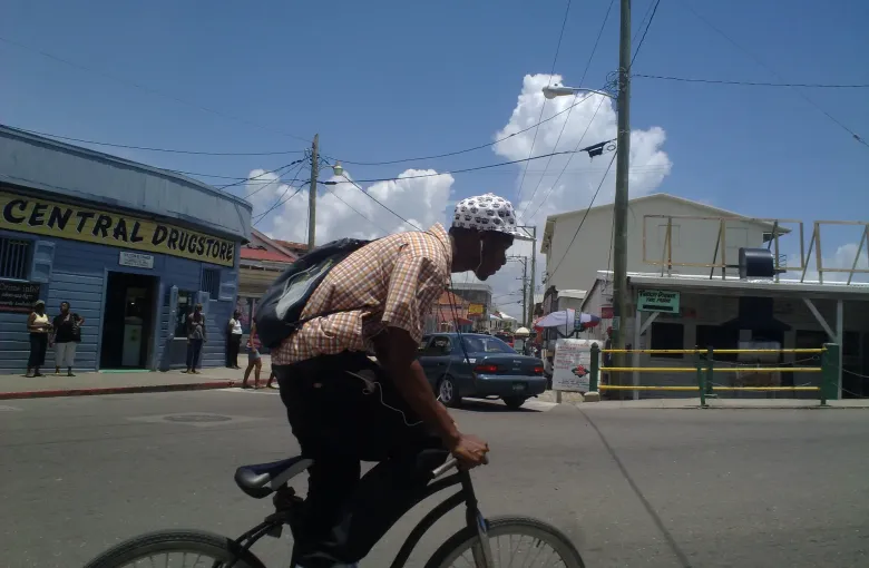A cyclist riding past the Central Drug Store on a Belize City street of low shopfronts.
