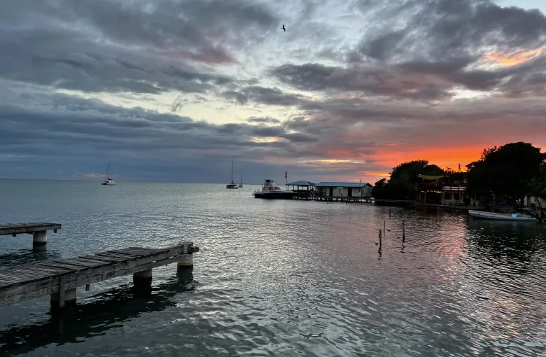 Heavy cloud breaking to orange over the water at Placencia, with a low wooden pier and moored boats.