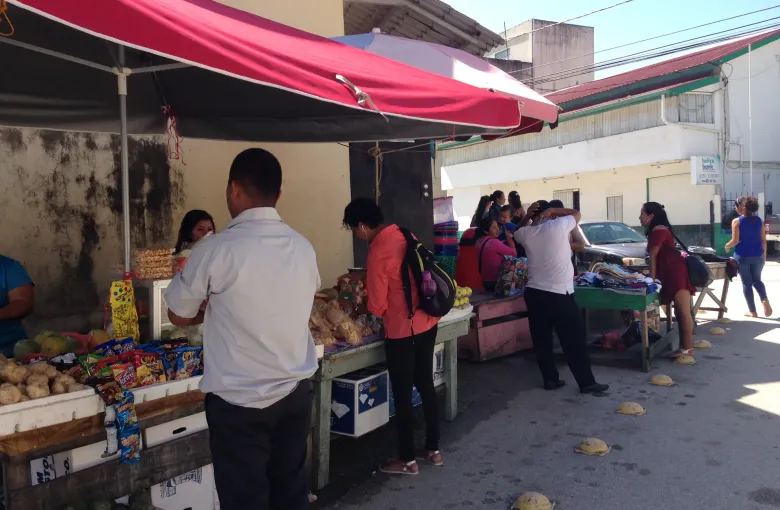 Shoppers at covered market food stands in San Ignacio, with crates of produce in the foreground.