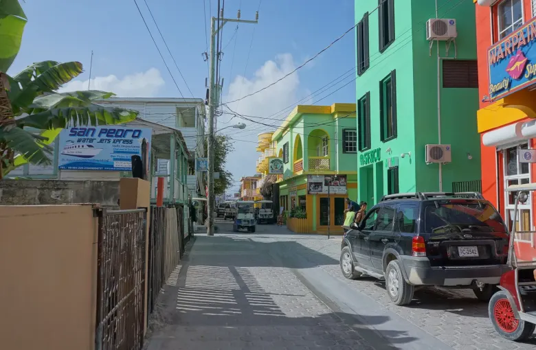 Brightly painted shopfronts in green, yellow and red along a narrow street in San Pedro, Belize.