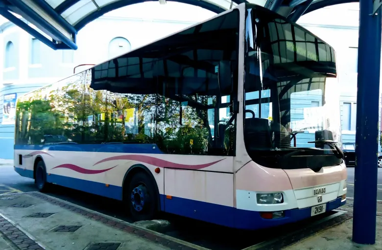 A pink and blue Bermuda public bus standing under the canopy at the Hamilton terminal.