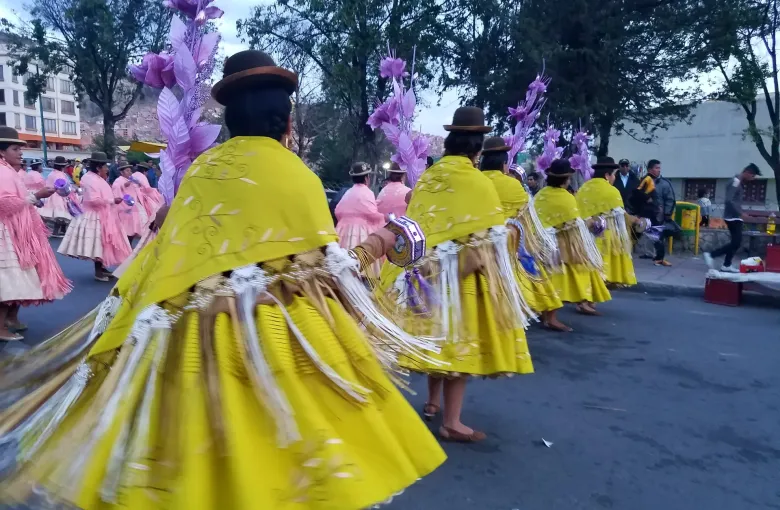 Women in bowler hats, embroidered shawls and full pollera skirts turn in a street procession in La Paz.