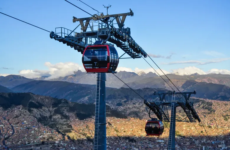 Two red cable car cabins of the Mi Teleferico red line cross above La Paz with the snow topped cordillera behind.
