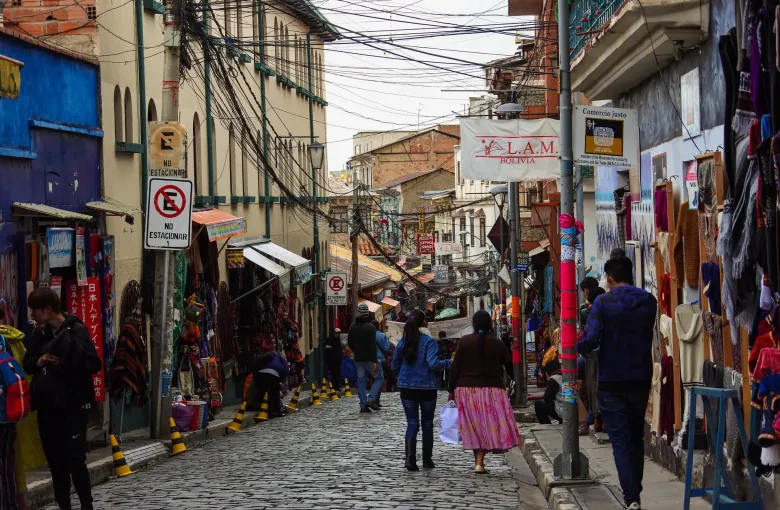Shoppers walk a steep cobbled street in La Paz lined with textile and alpaca stalls.
