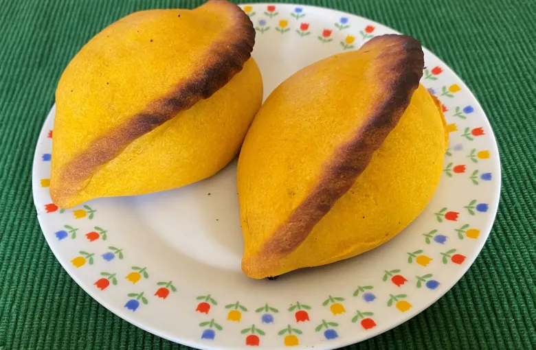 Two baked saltenas with their braided seam on a patterned plate.
