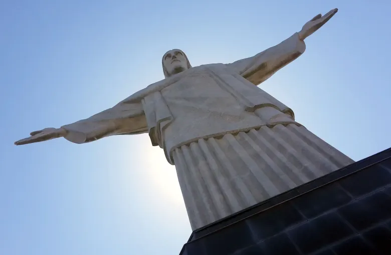 The Christ the Redeemer statue on the Corcovado seen from below with its arms outstretched against a clear sky.