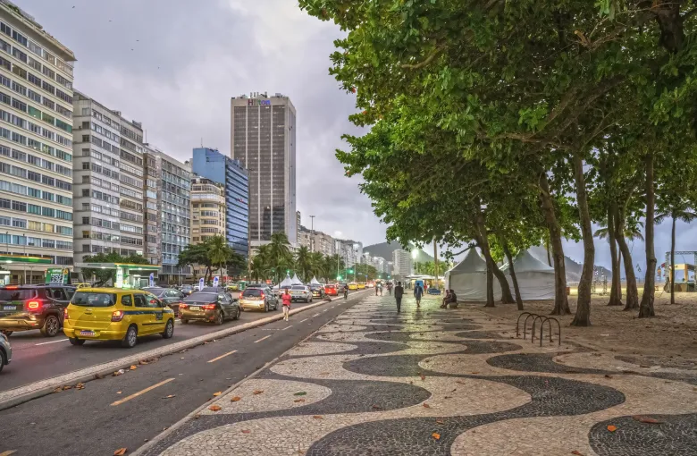 The wave-patterned mosaic promenade at Copacabana under a line of palms, with apartment blocks along the avenue.