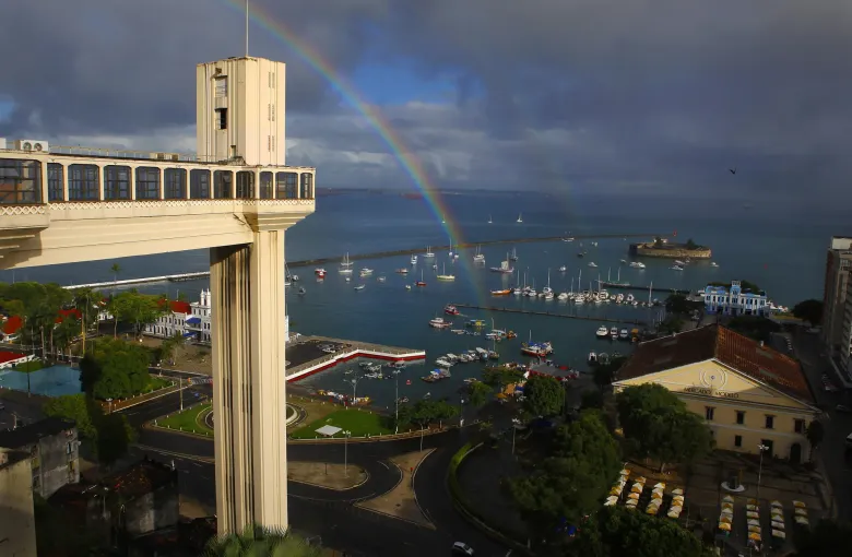 The Elevador Lacerda standing above the lower city and the harbour at Salvador, with a rainbow over the bay behind it.