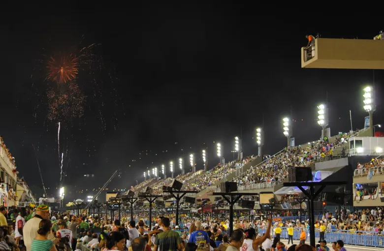The Sambadrome in Rio de Janeiro at night during a parade, the avenue lit between packed stands with fireworks above.
