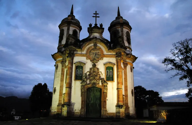 The twin towers and curved baroque facade of the church of Sao Francisco de Assis at Ouro Preto lit at dusk.