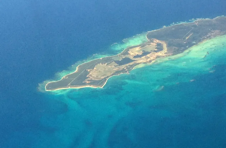 Anegada from the air: a low flat island ringed by pale reef and shallow turquoise water.