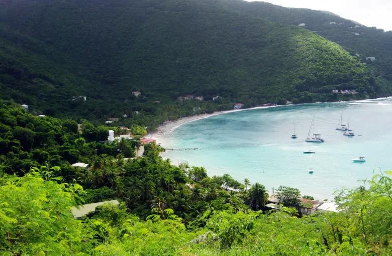 Green hills above Cane Garden Bay on Tortola, with sailing boats anchored in clear water offshore.