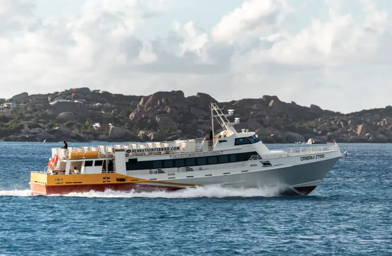 A passenger ferry running between the islands, with the boulder-strewn shore of Virgin Gorda behind it.