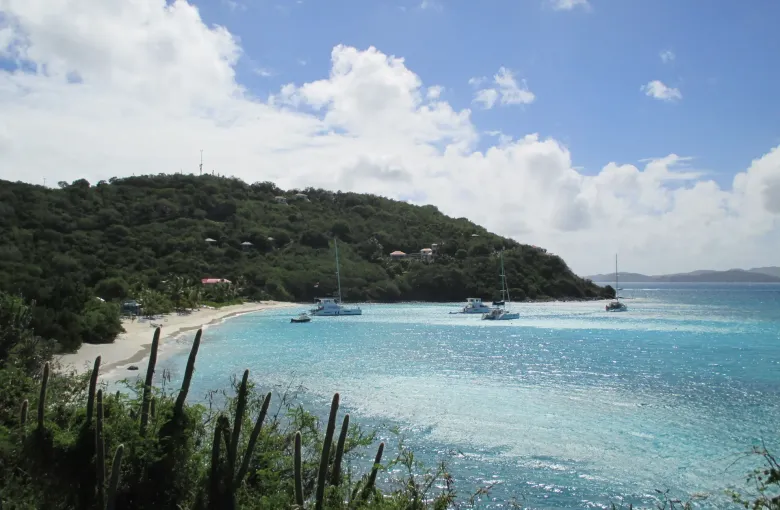 A sandy beach on Jost Van Dyke backed by green hills, with catamarans moored in shallow clear water.