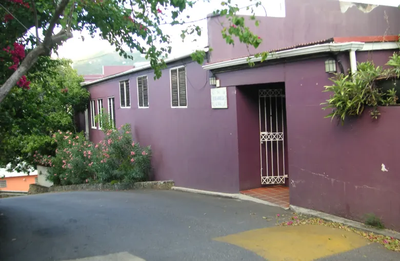 A magenta painted building on a Road Town corner, bougainvillea over the wall and shutters at the windows.