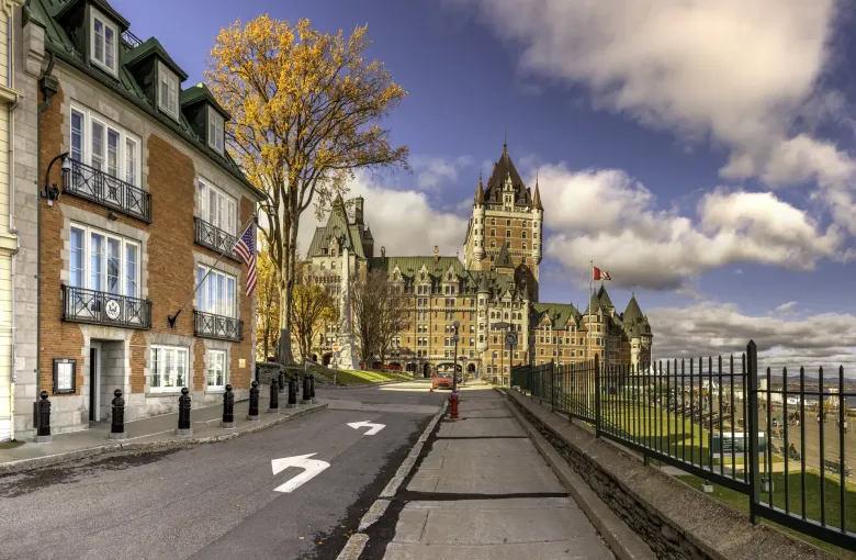 A turreted copper roofed hotel rising above a quiet street of brick and stone buildings, with an autumn maple in leaf.