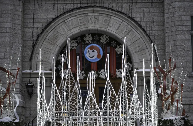 Paper snowflakes and a snowman emblem in the arch of a stone city hall, behind tall lit ice sculptures.