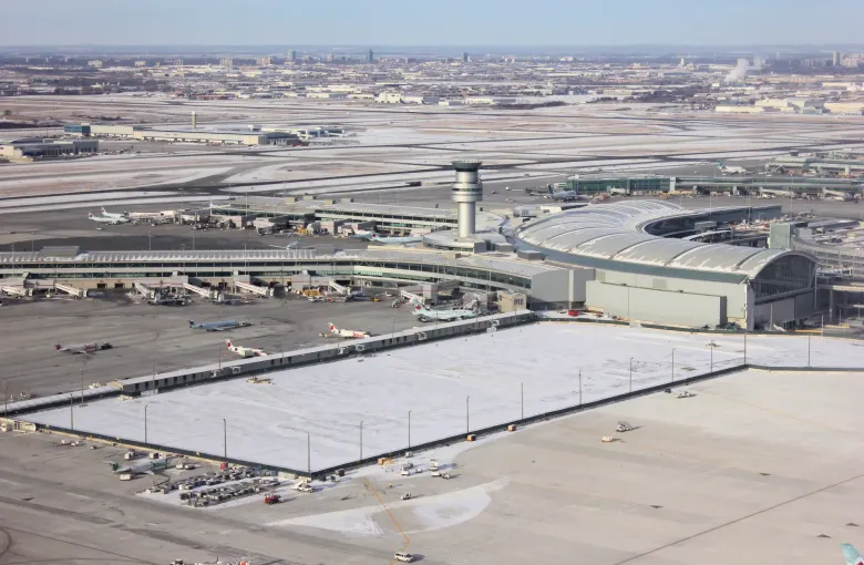 An aerial view of airport terminals and a control tower with aircraft at the gates and snow across the aprons.