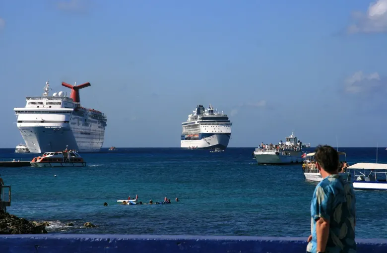 Two cruise ships anchored off George Town, with small tender boats ferrying passengers to the waterfront.