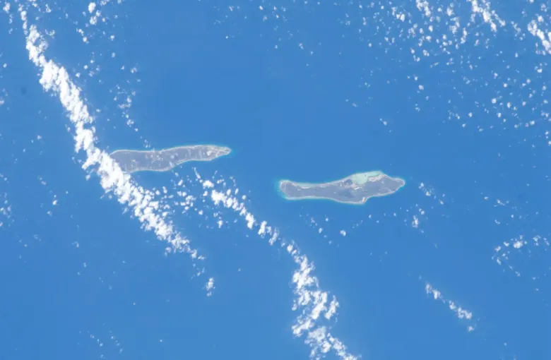 Little Cayman and Cayman Brac from orbit, two narrow islands ringed by pale shallows in deep blue sea.