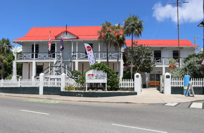 The white timber and stone National Museum in George Town, red roofed, with deep verandahs and a picket fence.