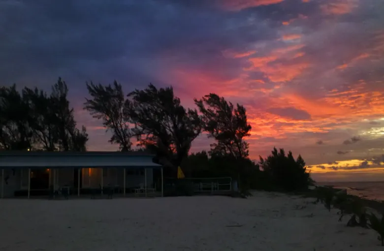Red and violet cloud at sunset over a quiet North Side beach on Grand Cayman, with trees in silhouette.