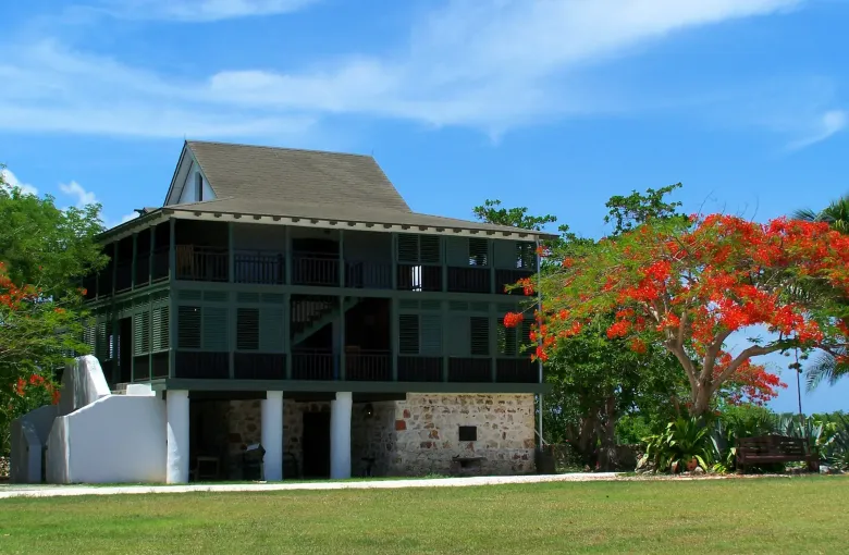 The restored three-storey great house at Pedro St. James, with deep shaded verandahs and a flame tree in red bloom.
