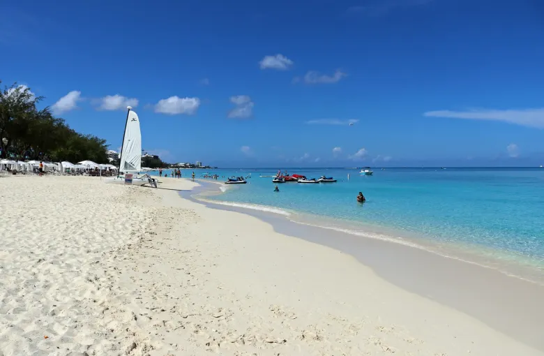 Sunloungers and a moored sailing boat on Seven Mile Beach, with bright turquoise shallows running south along the shore.