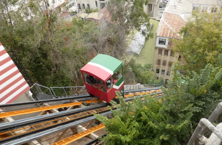 The red and green car of Ascensor El Peral descending its track above the rooftops of Valparaiso.