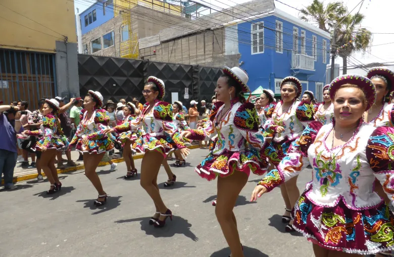 A troupe of caporales dancers in embroidered costume and round hats moving along the street at the Carnaval Andino in Arica.