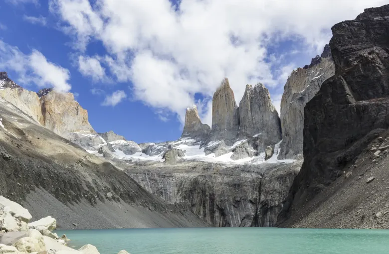 The three granite towers of Paine rising above a turquoise glacial lake ringed by scree in Chilean Patagonia.
