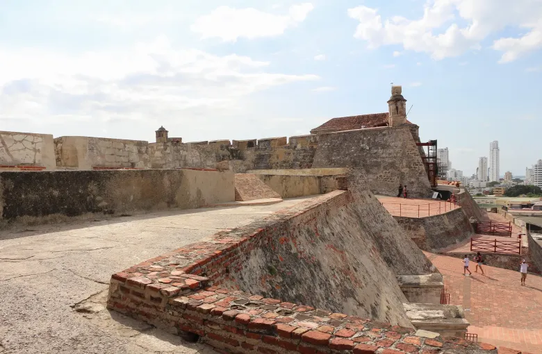 The stone ramparts and sloping batteries of the Castillo San Felipe de Barajas in Cartagena, with the modern city skyline beyond.